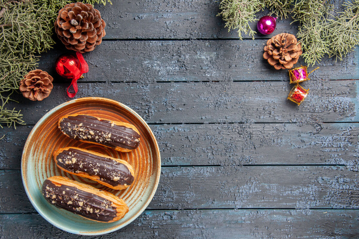 地面俯视图巧克力eclairs上的椭圆形板松果圣诞玩具冷杉树叶上的黑色木质地面与复制空间松果顶部棕色