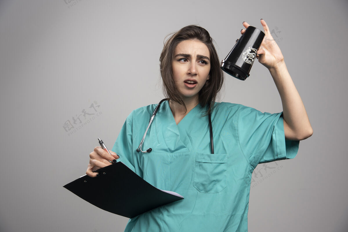 剪贴板疲惫的医生拿着杯子和剪贴板在灰色背景上高质量的照片健康医生诊所