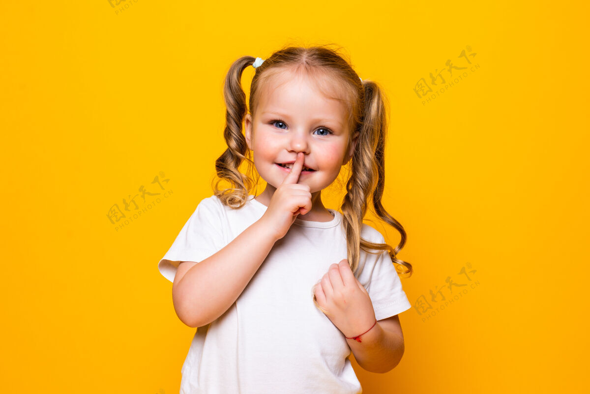 沉默小女孩用手指捂着嘴说嘘隔离黄墙可爱微笑编织