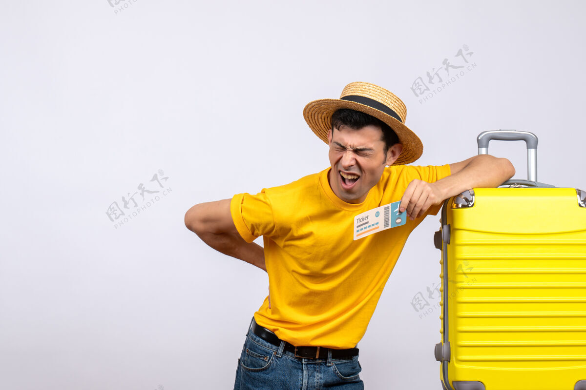 抱正面图：年轻的游客站在黄色手提箱旁 痛苦地背着他的背站男视图
