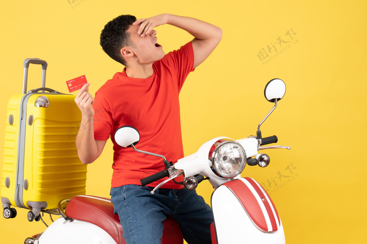 信用卡前视图骑着轻便摩托车的年轻人拿着信用卡把手放在脸上男人轻便摩托车信用卡