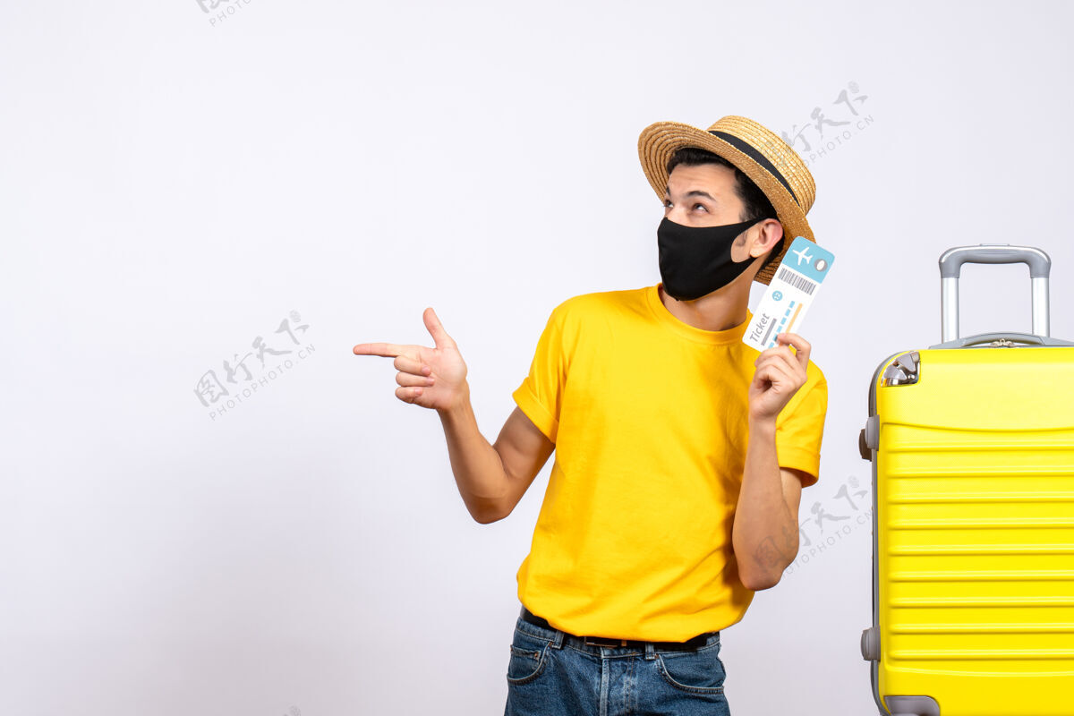站立正面图穿着黄色t恤的年轻人站在黄色手提箱旁 拿着旅行票指着左边旅行视图休闲