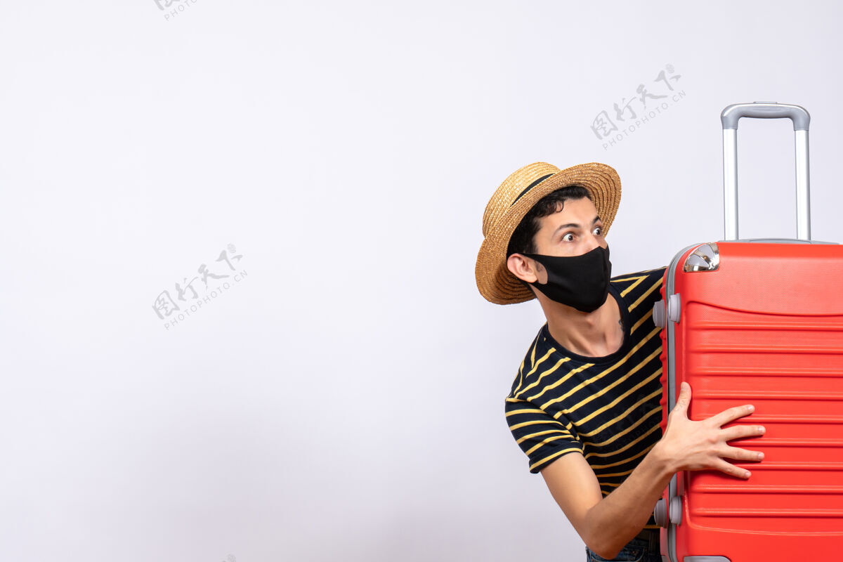人正面图是一个戴着黑色面具 躲在红色手提箱后面 忧心忡忡的年轻游客盖一前