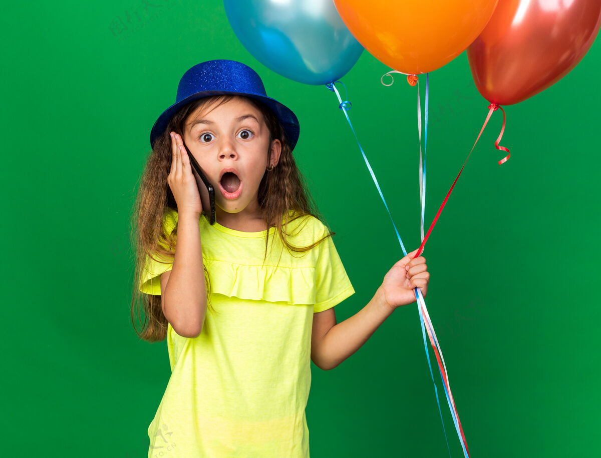 氦惊讶的白人小女孩 戴着蓝色派对帽 手里拿着氦气球 在绿色墙壁上讲着电话 还有复印空间聚会白种人女孩