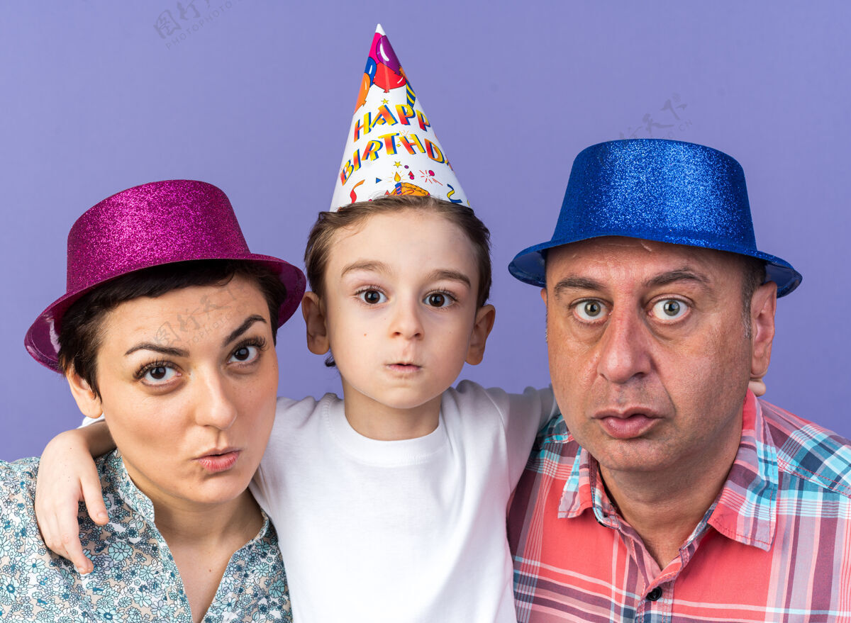 帽子焦急的母亲和父亲戴着聚会帽 和他们的儿子孤零零地站在紫色的墙上站着父亲孤独