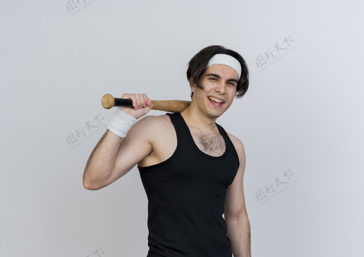 穿着一个穿着运动服 头戴棒球棒的年轻人站在白色的墙上 面带微笑 眨着眼睛看着前方眨眼棒球站着