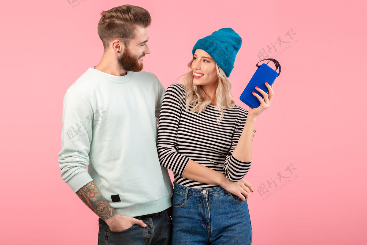 享受一对年轻夫妇穿着时尚的服装 穿着粉色的衣服 在无线扬声器上听音乐科技男人时尚