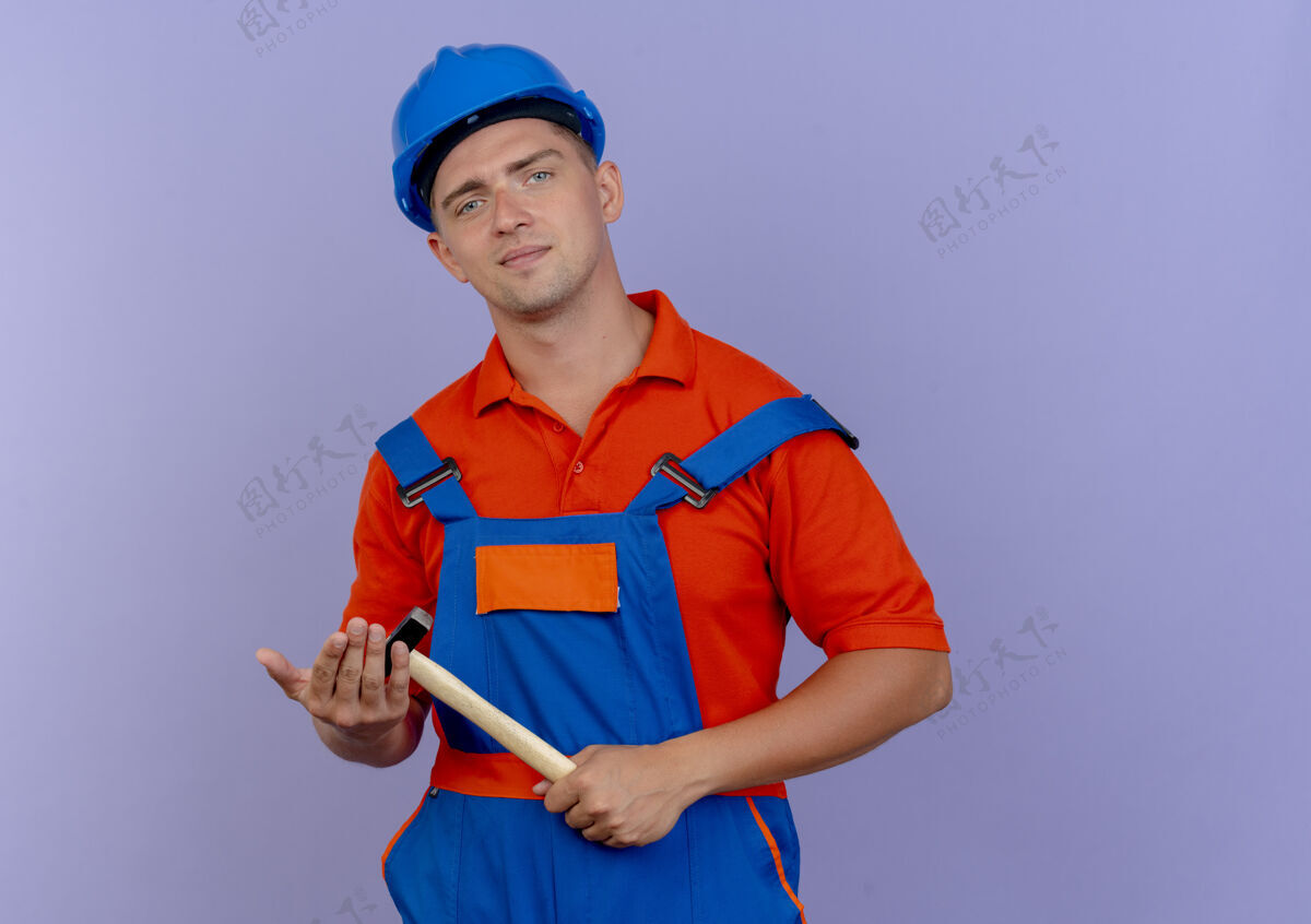 背景高兴的年轻男性建筑工人穿着制服和安全帽手持铁锤男性紫色请拿着