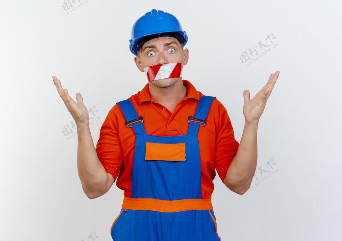 密封年轻的男建筑工人穿着制服 戴着安全帽 用胶带封住嘴巴 摊开双手年轻胶带背景