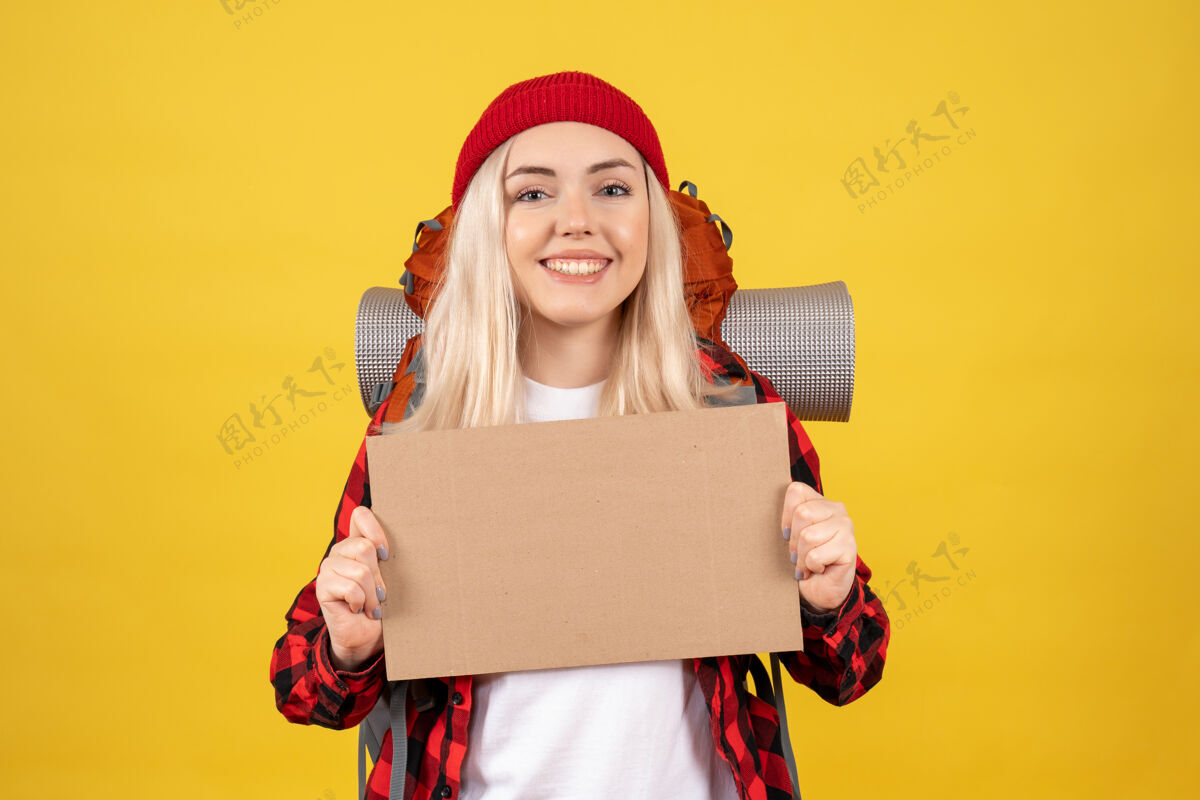 帽子正面图年轻的旅行女孩戴着红帽子拿着纸板站在黄色的墙上女士站着硬纸板