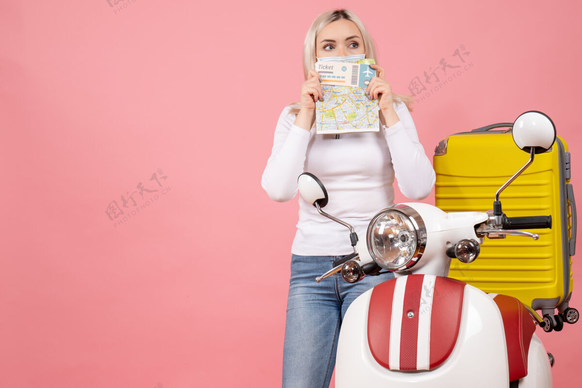 小姐前视图年轻女士举着车票和地图站在轻便摩托车旁边举行轻便摩托车快乐