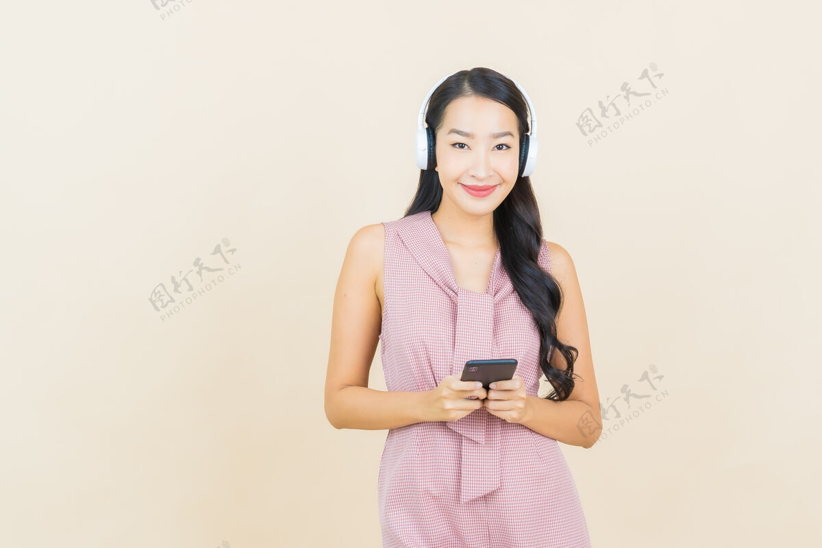 耳机戴着耳机和智能手机听音乐的美丽亚洲年轻女子肖像休闲耳机音乐