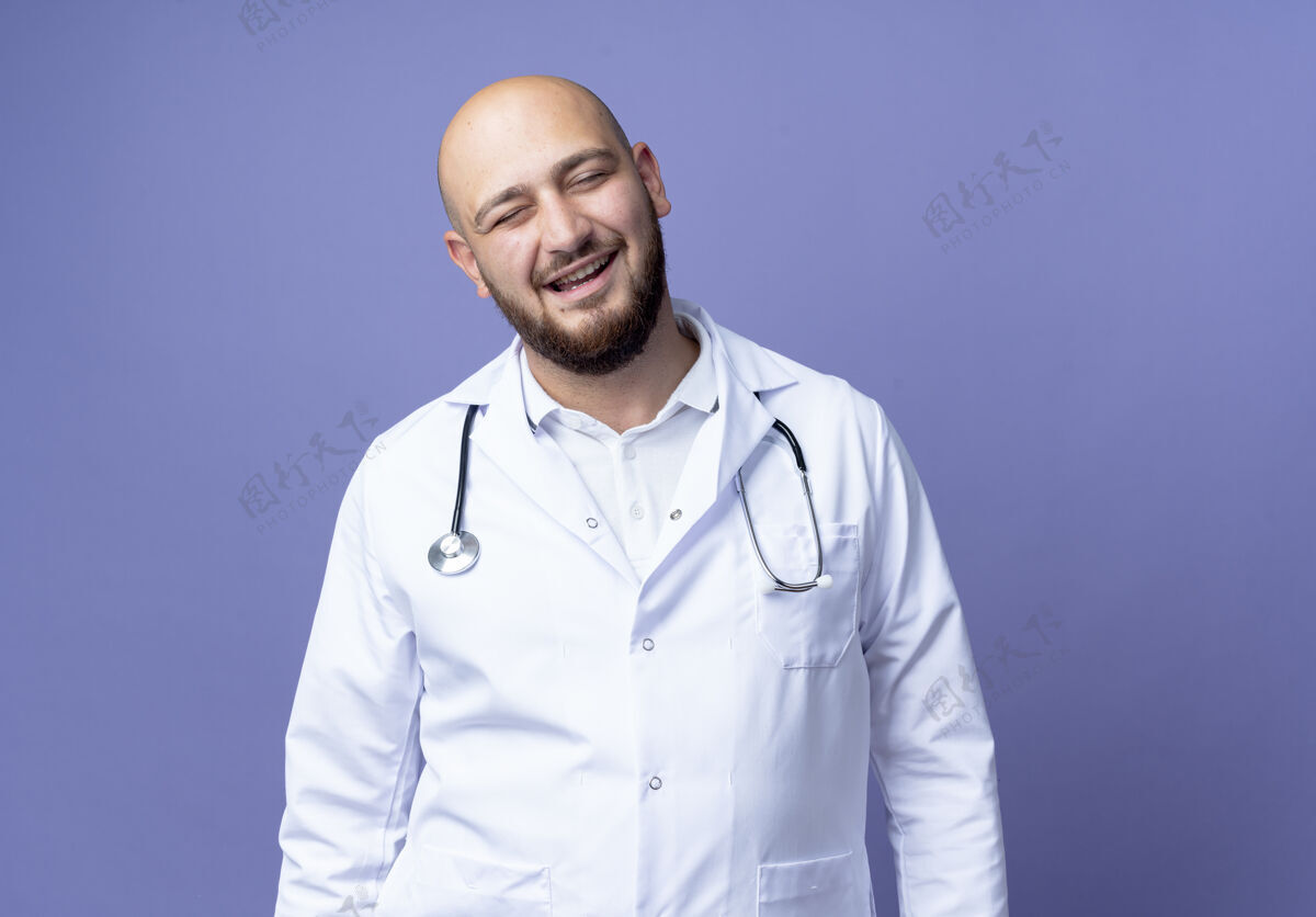 长袍高兴的年轻秃头男医生穿着医用长袍和听诊器-秃头年轻听诊器