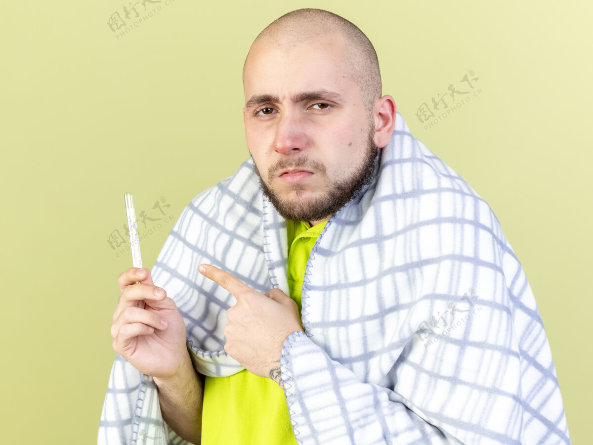 橄榄一个穿着格子布的年轻病患 拿着一只手 看着隔离在橄榄绿墙上的温度计疾病表情人