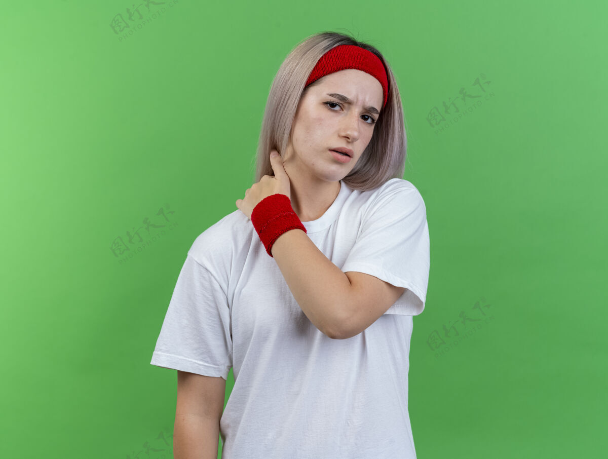 头带戴着护腕 戴着头带 手放在脖子上 孤零零地站在绿色的墙上运动年轻腕带