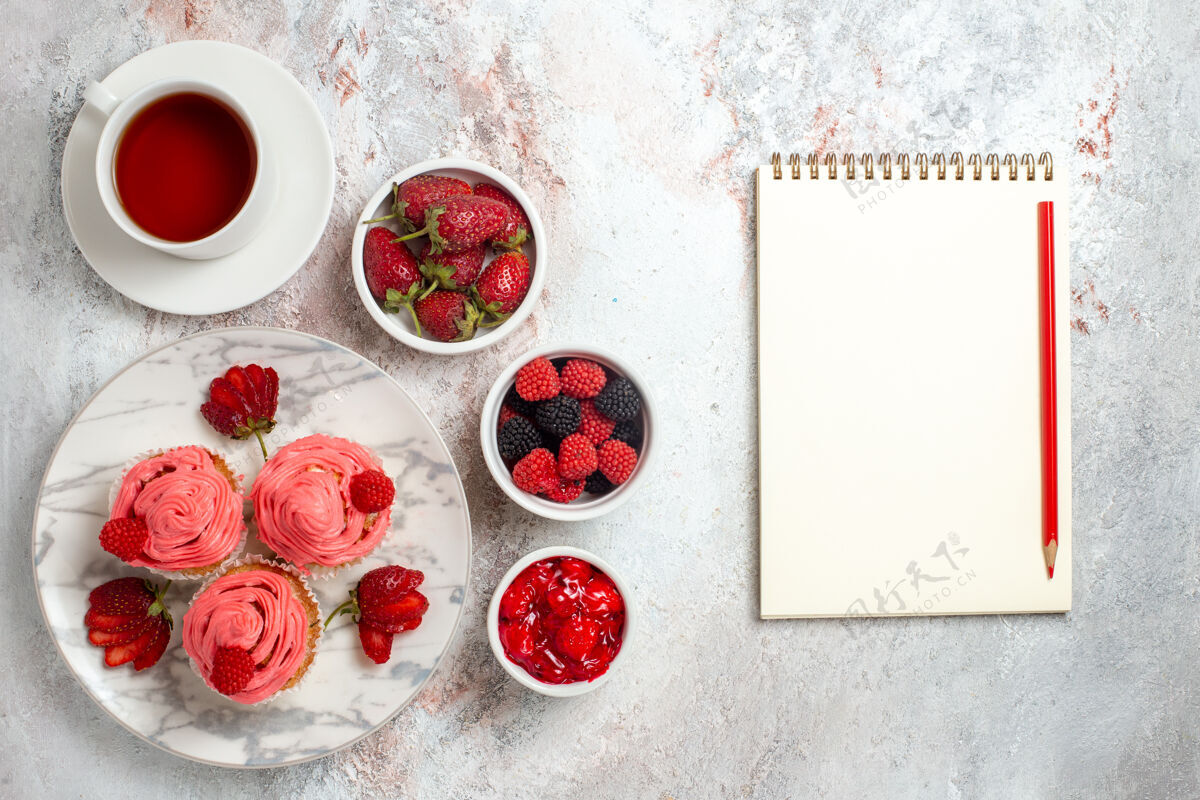 盘子白色表面上的粉红色草莓蛋糕和一杯茶的俯视图水果茶饼干