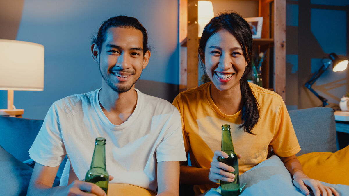视频通话快乐的亚洲年轻夫妇享受夜晚聚会活动坐在沙发上与朋友视频通话沙发成人亚洲人