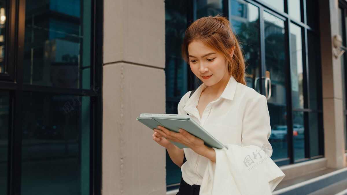 高管成功的亚洲年轻女商人穿着时尚的办公服 使用数码平板电脑和打字短信步行自信应用程序