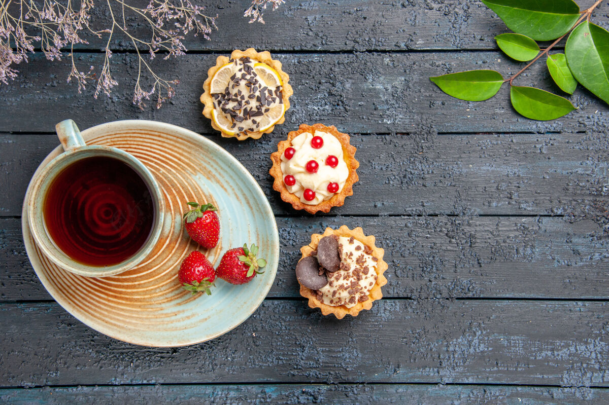 木头顶视图一杯茶和草莓放在茶托馅饼上 叶子和干花枝放在深色的木桌上早餐盘子健康