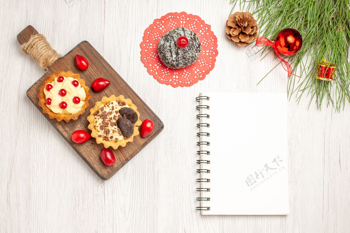 书签俯瞰砧板上的可可 浆果馅饼和山茱萸可可蛋糕和松树叶子 还有白色木质地面上的圣诞玩具和笔记本松树圣诞树笔记本