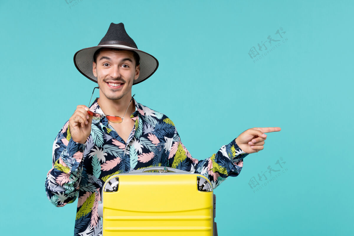 包一个年轻的男人正拿着他的黄色袋子准备旅行 指着蓝色的墙上假期指向准备