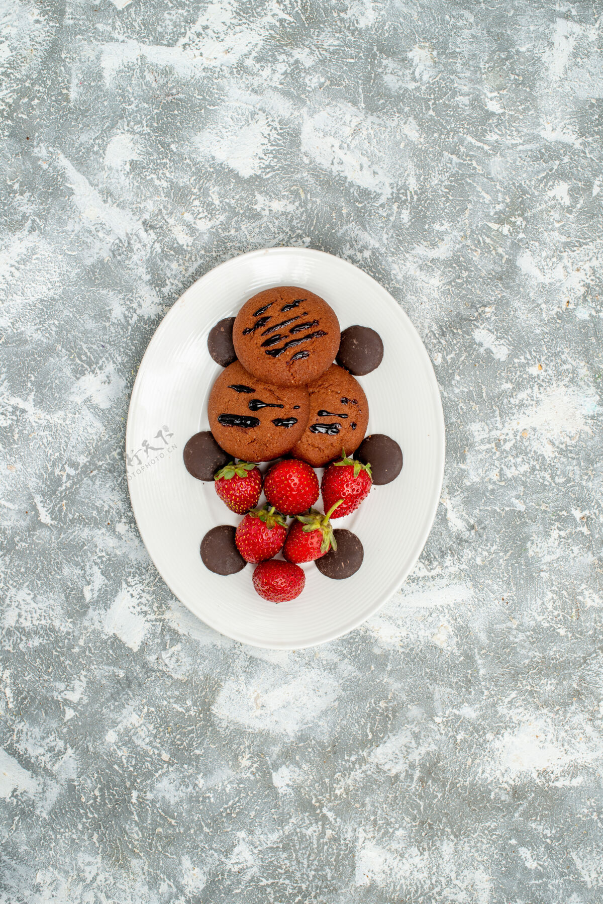盘子顶远景巧克力饼干草莓和圆巧克力在白色椭圆形盘子上的灰白色地面甜点蓝莓红醋栗