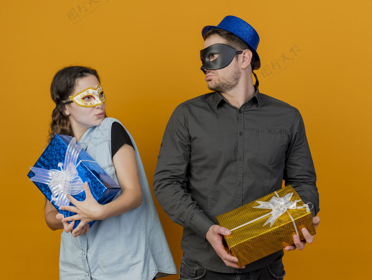 盒子未出柜的年轻派对情侣手拿礼盒 戴着化装眼罩 彼此看着橙色隔离化装舞会穿每个
