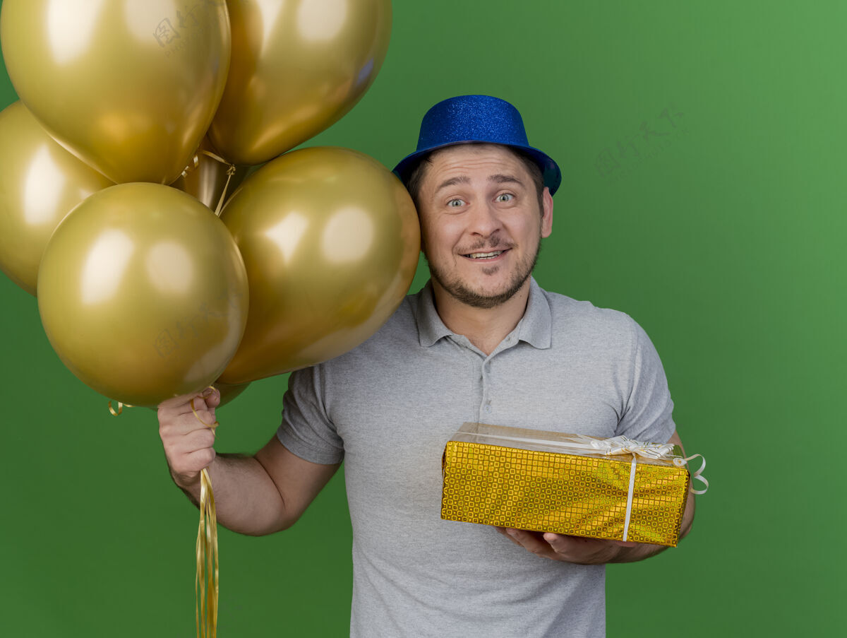 礼物微笑的年轻人戴着派对帽拿着气球和礼品盒隔离在绿色派对拿着绿色