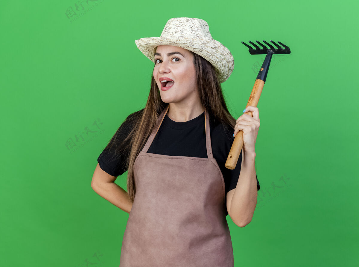 制服印象深刻的美丽的园丁女孩穿着制服戴着园艺帽提高耙隔离在绿色帽子穿提高
