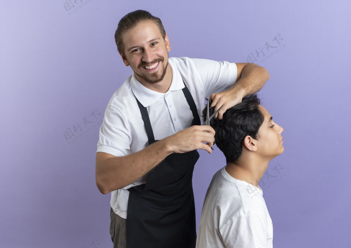 帅气微笑的年轻英俊的理发师穿着制服 在紫色的墙上为年轻的客户理发姿势脸客户