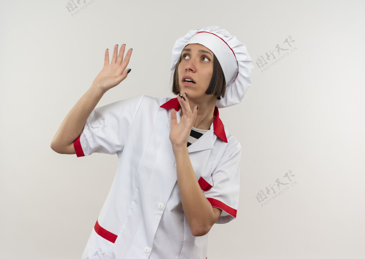人身穿厨师制服的年轻女厨师被吓得两手空空地站在白色的墙上看着一边姿势人壁板