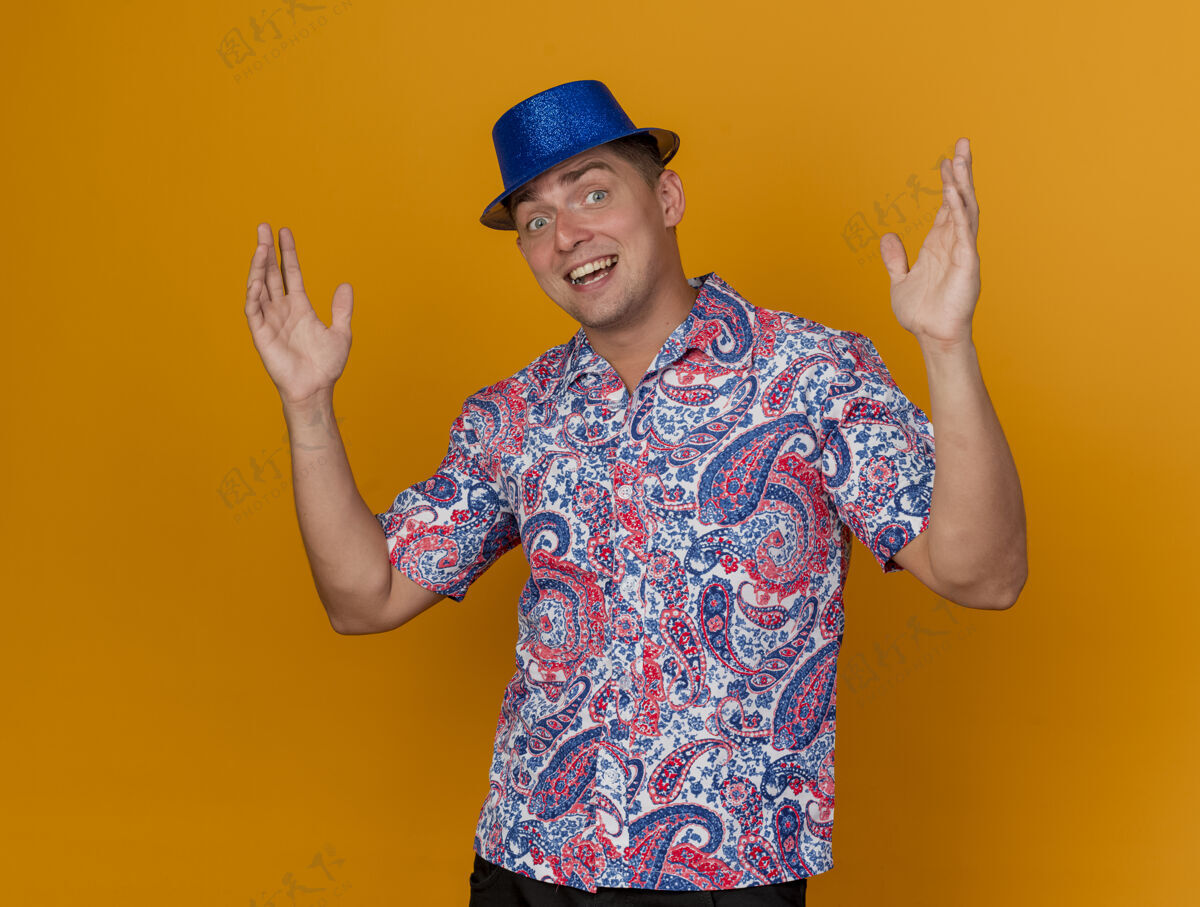 小伙子微笑着的年轻人戴着蓝色的帽子摊开双手孤立在橙色的党派对橙色穿