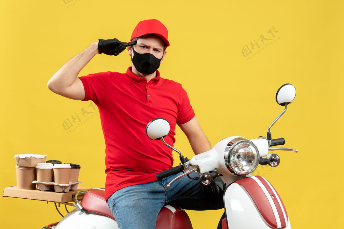 黄色前视图是一个情绪化的年轻人 穿着红色上衣 戴着帽子 戴着手套 戴着医用面罩 坐在黄色背景上的滑板车上传递命令摩托车摩托车思考
