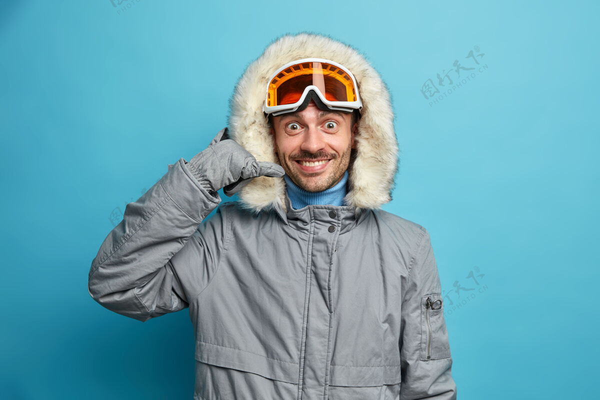 季节快乐的男滑雪运动员穿着带兜帽的冬季夹克 打电话的姿势积极地微笑着休闲年轻人穿