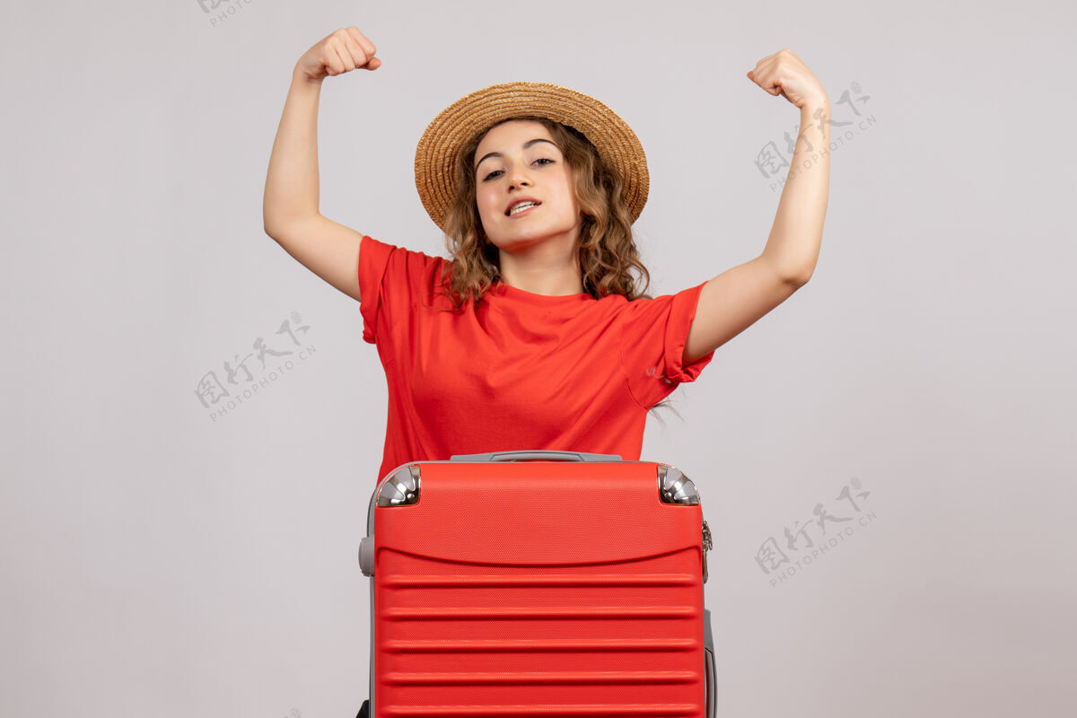 漂亮假日女孩的正面图 她的手提包显示手臂肌肉站在白色的墙上站可爱节日女孩