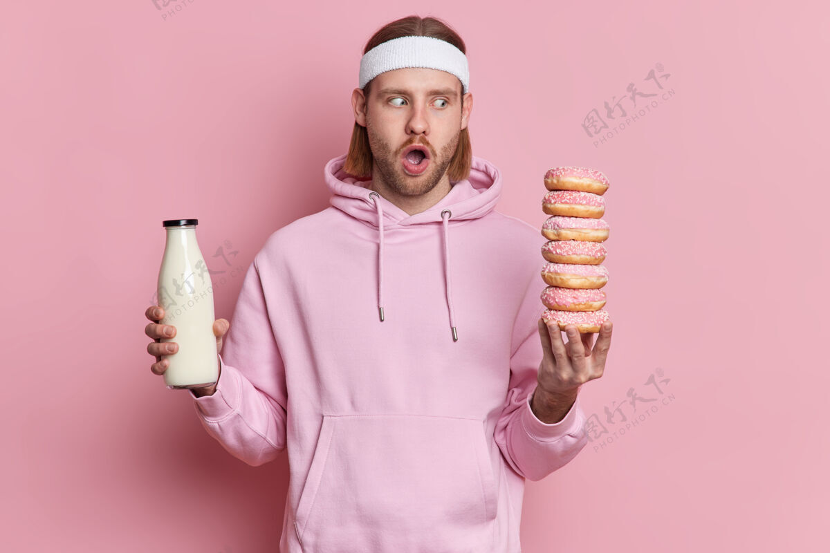凝视惊讶的运动型男人盯着美味的甜甜圈 穿着连帽衫 戴着白色的头巾 正准备吃呢垃圾健身运动员