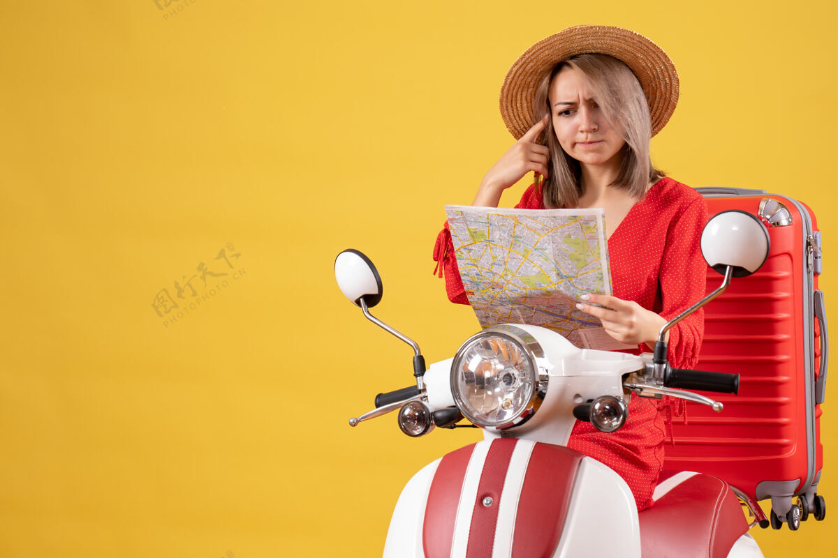 肖像前视图混乱漂亮的女孩骑着轻便摩托车与大手提箱举行地图人帽子举行