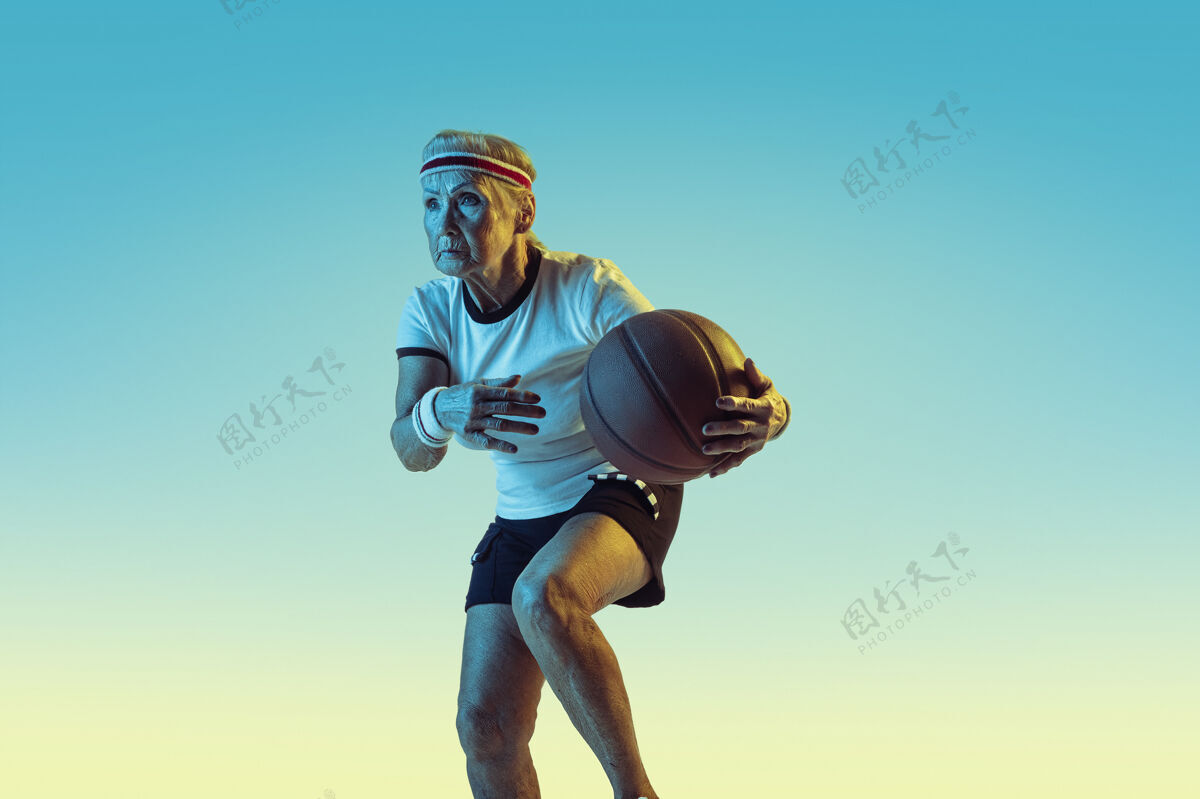 教练运动装的高级女性在渐变背景下打篮球 霓虹灯身材匀称的女性模特保持活跃运动 活动 运动 健康 自信的概念复制空间发球老年人球
