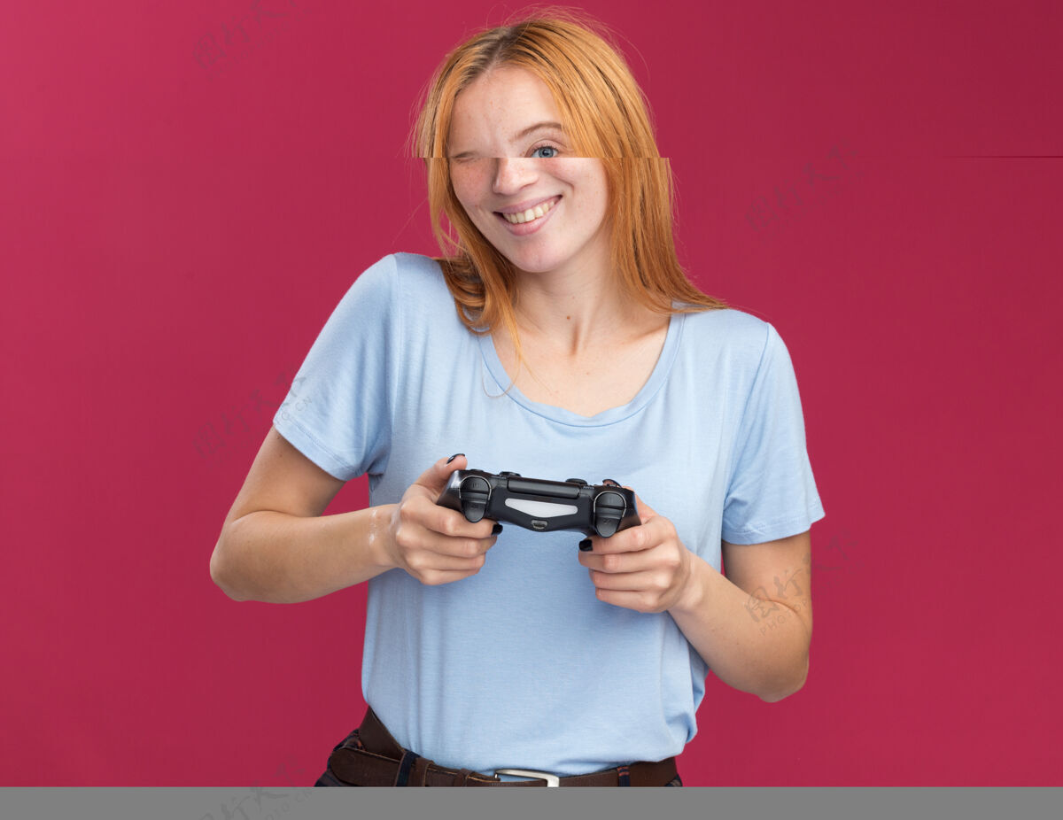 红发带着雀斑的年轻红发姜女微笑着拿着粉色的游戏控制器雀斑姜粉红