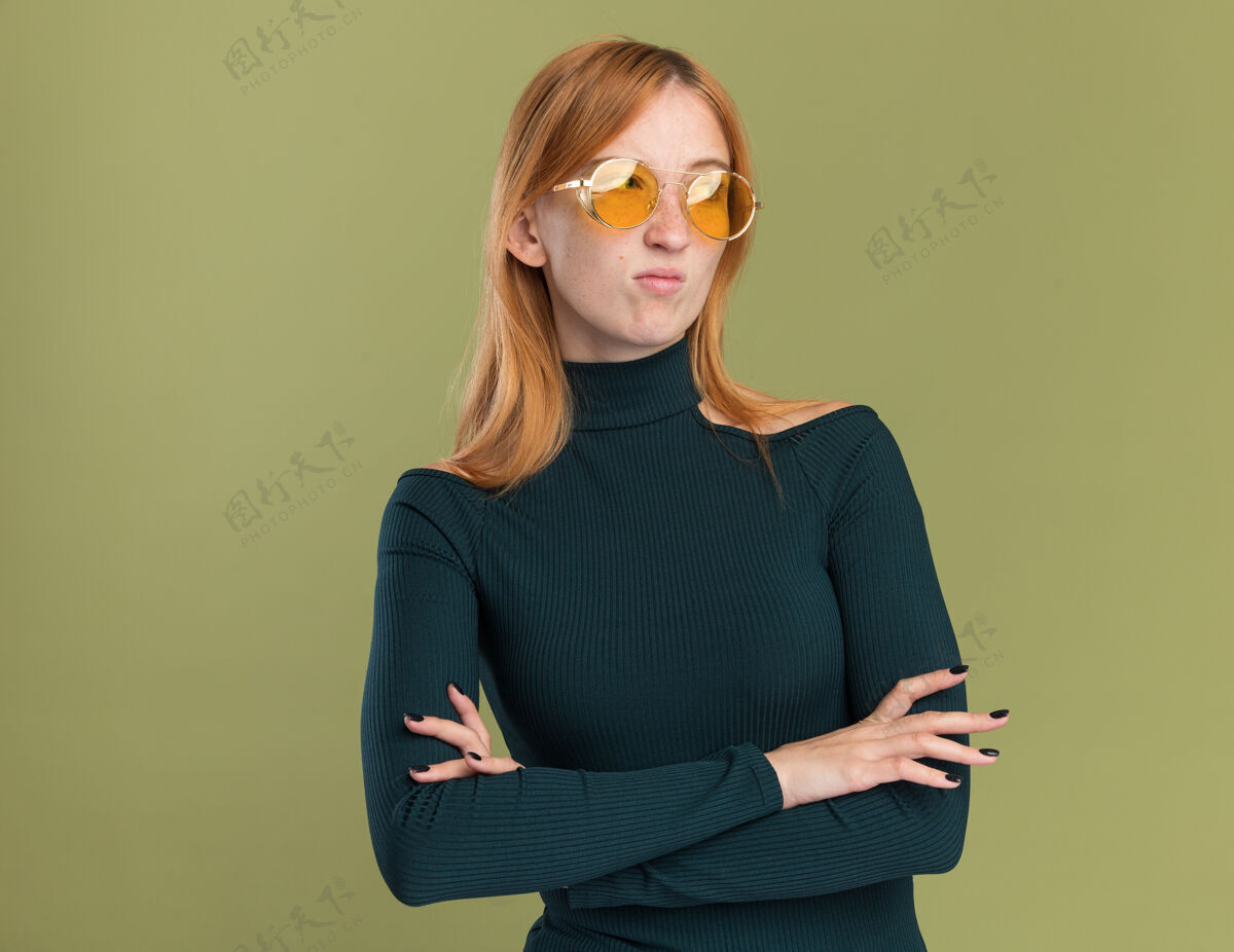 太阳戴着太阳镜 满脸雀斑的年轻红发姜黄色姑娘 双臂交叉站着 望着橄榄绿的一边壁板姜眼镜