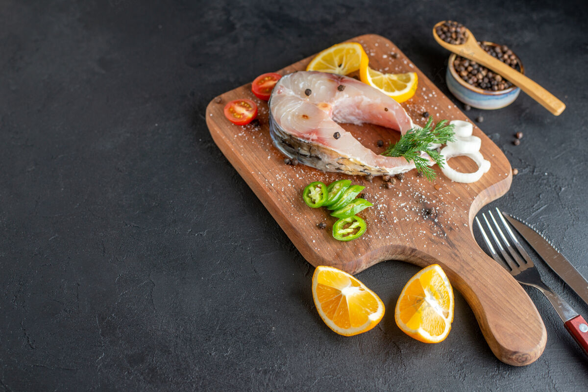 盘子侧视图生鱼肉和新鲜切碎的蔬菜柠檬片香料在一个木板餐具设置在黑色苦恼的表面生鱼排骨柠檬