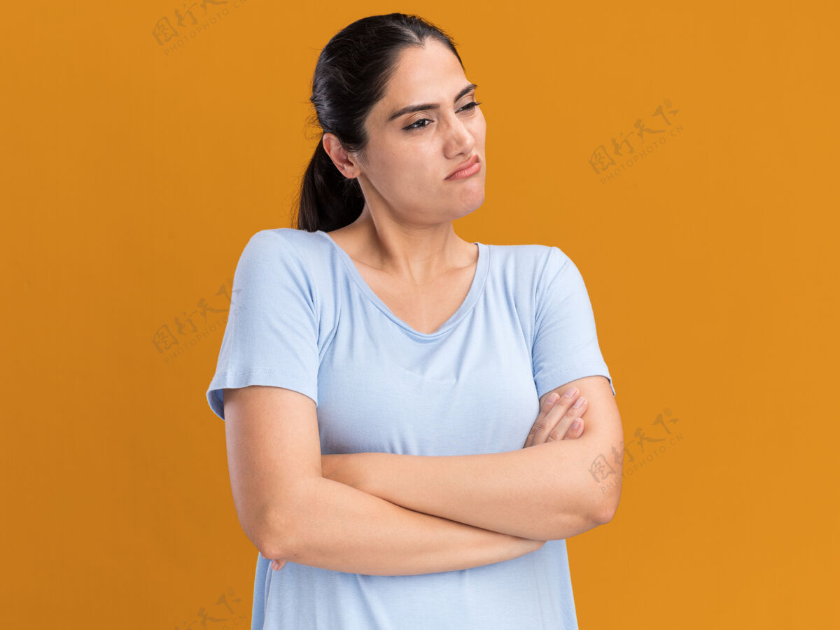侧线恼怒的年轻黑发白人女孩交叉双臂站在橙色的一边看着站立女孩手臂