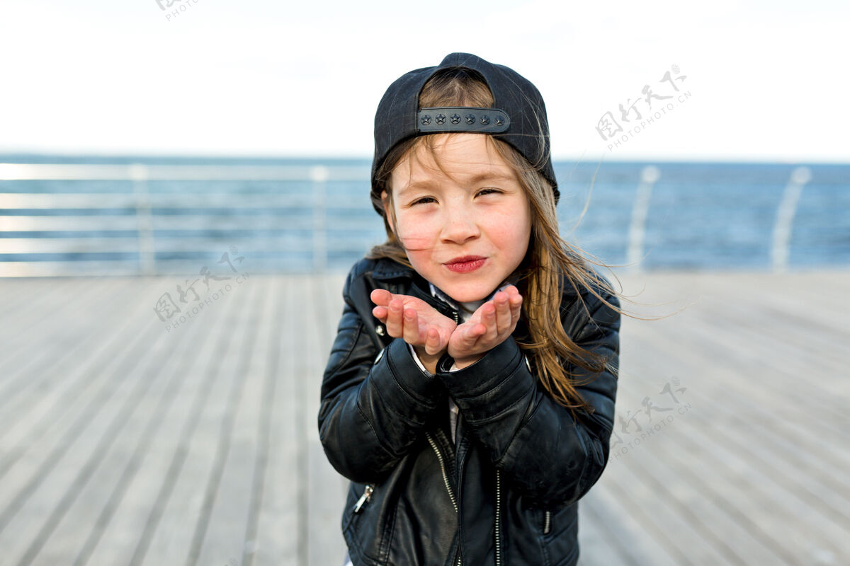 户外可爱可爱的小女孩穿着时髦的夹克和帽子送一个吻积极朋友友谊