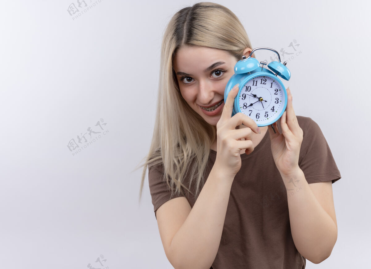 时钟带着牙套微笑的金发女孩 拿着闹钟 站在一片空白的空间里牙套闹钟金发