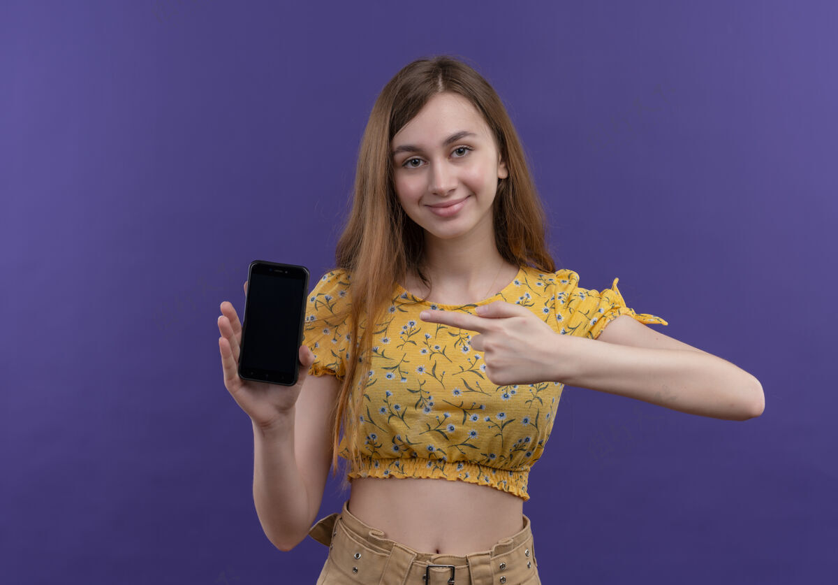 女孩高兴的年轻女孩拿着手机 指着它在孤立的紫色空间手机年轻紫色