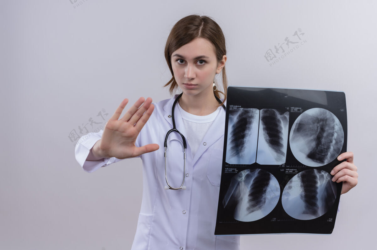 长袍面容严肃的年轻女医生 穿着医用长袍 手持听诊器 手持x光片做停车标志听诊器医疗严重