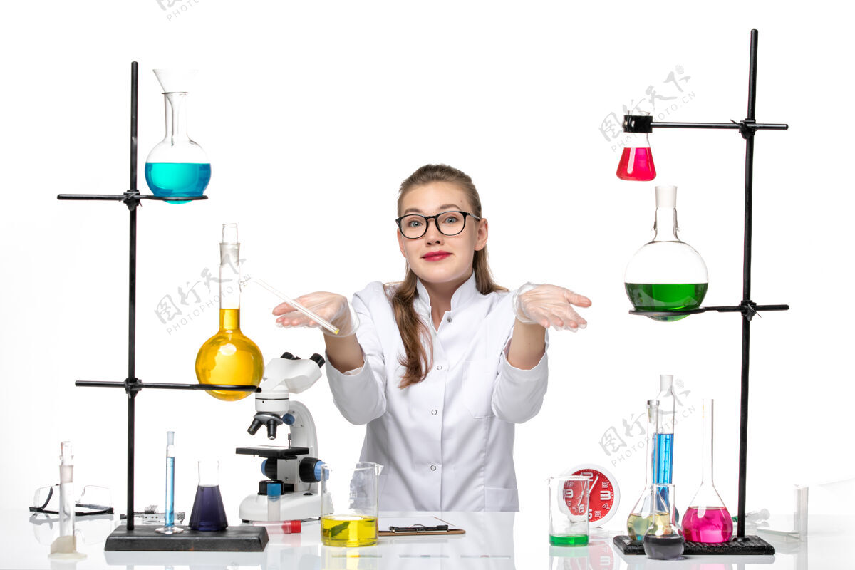 医生前视图穿着白色医疗服的女医生正坐在桌子前 用白色背景上的解决方案病毒冠状病毒大流行化学桌子女医生科学