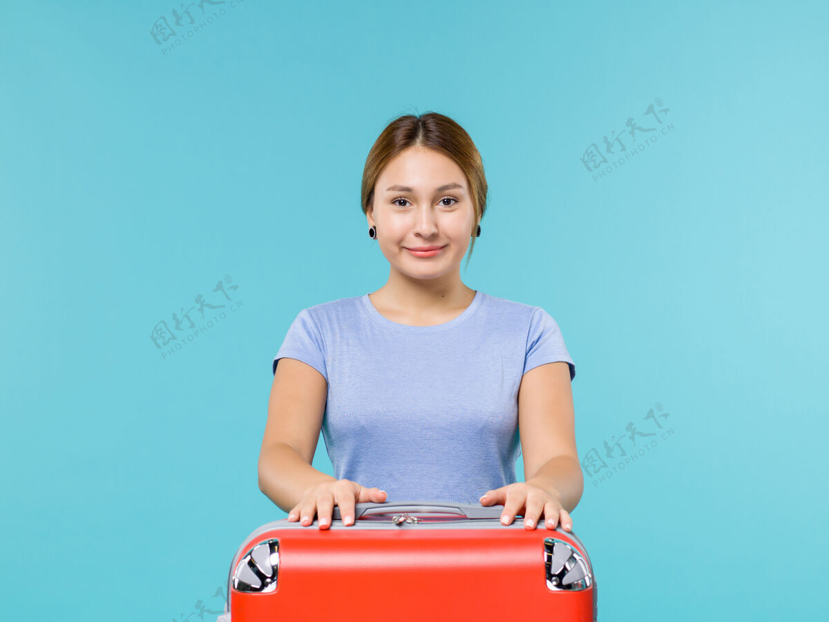 成人正面图：度假中的女性 带着她的红色袋子 在蓝色的背景上微笑 度假飞机旅行 航海旅行风景旅行前面