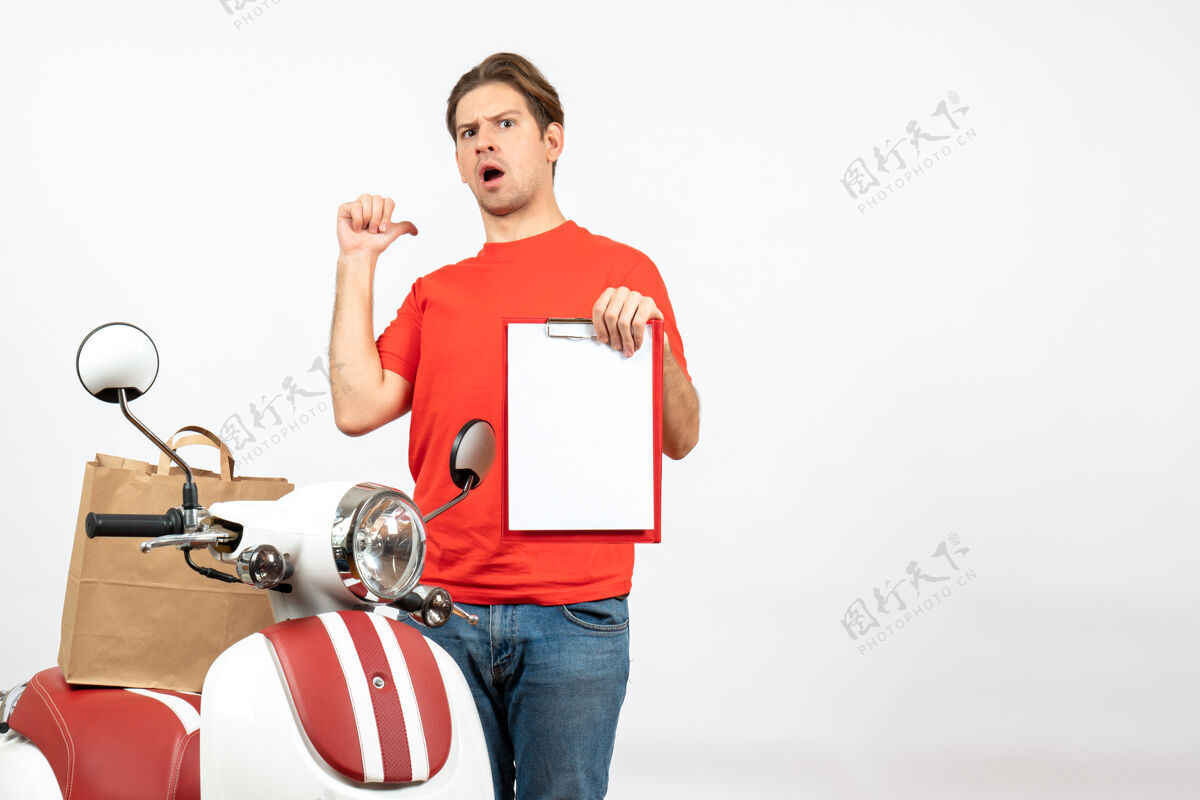 背部俯视图中 身穿红色制服的年轻送货员站在滑板车旁 显示文件指向白色墙上的背面人年轻运动装