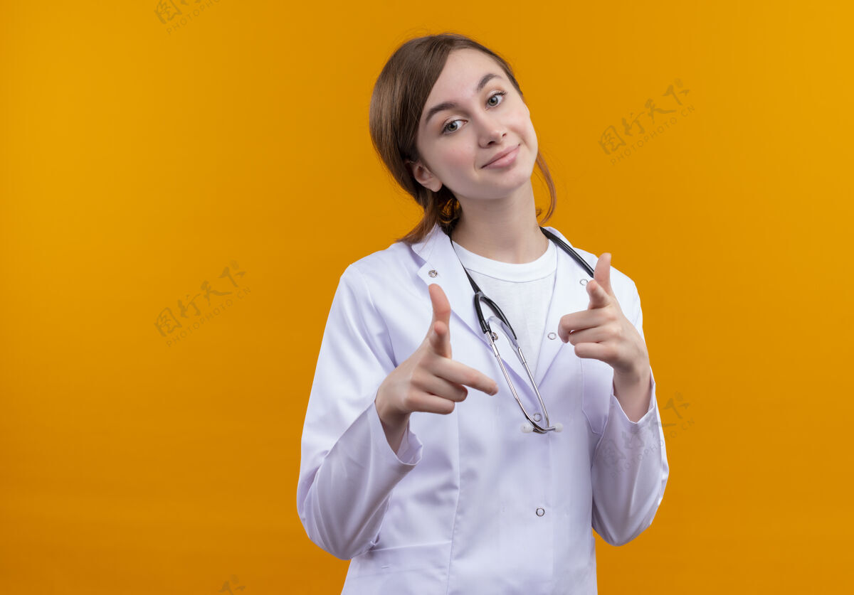 长袍高兴的年轻女医生穿着医用长袍和听诊器做你的手势在孤立的橙色空间与复制空间橙色穿医生